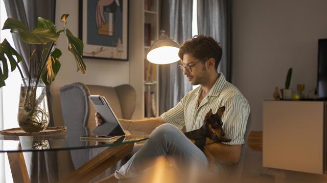 En man läser information på sin Ipad hemma med sin hund i knät. 